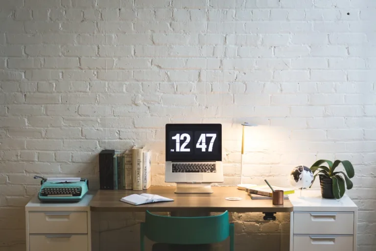 Home desk with a laptop showing 12:47 beside books and a lamp, ready for calls across long-distance relationship time zones